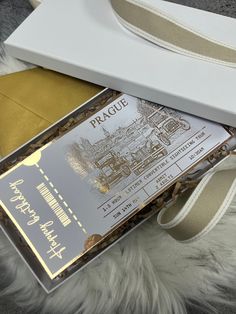 a white box with a silver and gold label on it next to a beige ribbon