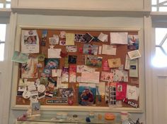 a bulletin board covered in pictures and papers on the side of a wall next to a window