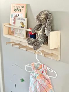 a stuffed animal is sitting on a wooden shelf next to a book rack and clothes