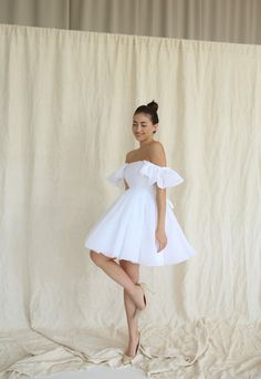 a woman in a short white dress posing for the camera with her legs spread out