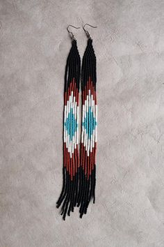 two long beaded earrings with red, white and blue designs on them sitting on a gray surface