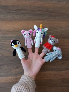 someone is holding their hand up with five small knitted animal finger puppets in front of them