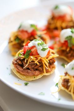 mini tacos with meat, cheese and tomatoes on them sitting on a white plate