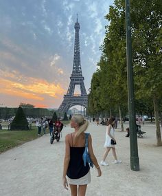 a woman is standing in front of the eiffel tower at sunset or dawn