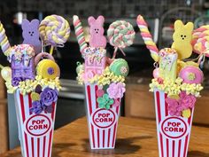 three popcorn buckets filled with candies and lollipops on top of a table