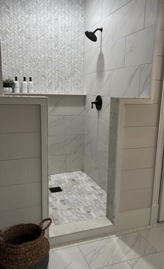 a walk in shower sitting next to a white tiled wall and floor with a basket on the side