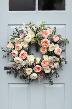 a wreath on the front door with flowers and greenery hanging from it's sides