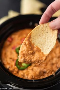 a hand holding a tortilla chip over a bowl of salsa