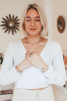 a woman with blonde hair wearing a white shirt and holding her hands together in front of her chest