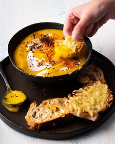 a person dipping some kind of food in a bowl with bread and butter on the side