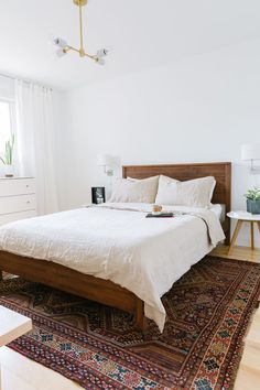 a bed with white sheets and pillows on top of a rug in a bedroom next to a window