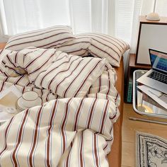 a laptop computer sitting on top of a bed next to pillows and blankets in front of a window