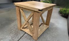 a small wooden table sitting on top of a cement floor next to potted plants