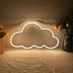 a cloud shaped neon light sitting on top of a bed next to flowers and vases