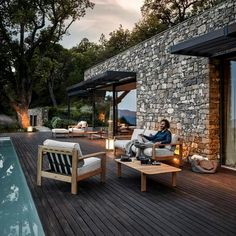 a man sitting on a chair next to a table near a swimming pool at dusk