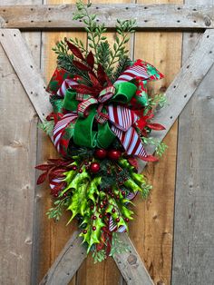 a christmas wreath hanging on the side of a wooden fence with green and red ribbons