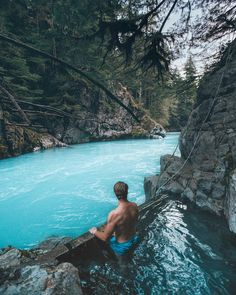 a man sitting on rocks in the middle of a river with blue water and trees around him