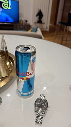 a can of red bull next to a watch on a table in front of a tv