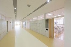 an empty hallway with lockers and tables in the center, leading to another room