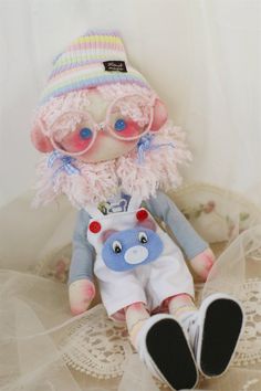 a small stuffed animal with pink hair and blue eyes sitting on a lace doily