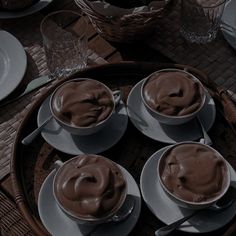 there are four cups of hot chocolate on the table with plates and utensils