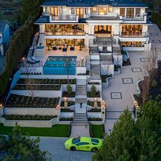 a green car is parked in front of a large house with an outdoor swimming pool