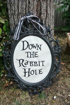 a sign that says down the rabbit hole on it's side next to a tree