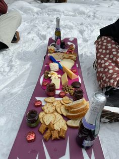 a table topped with cheese and crackers next to a bottle of wine in the snow