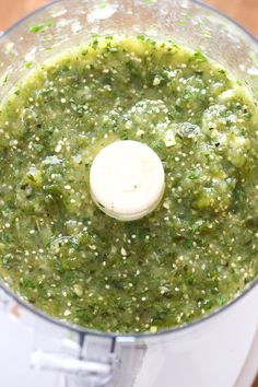 a food processor filled with green sauce on top of a wooden table