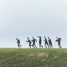 a group of people running across a grass covered field in the shape of a line