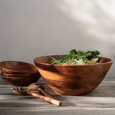 two wooden bowls filled with green salad on top of a table next to utensils