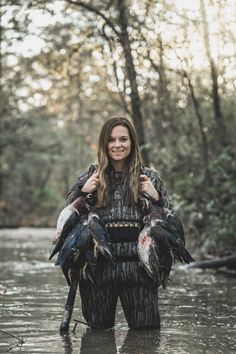 a woman holding two birds in her hands while standing in the middle of a river