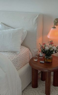 a bed with white linens and flowers on the night stand next to a small table