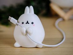 a little white bunny holding a charger on top of a wooden table