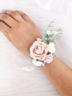 a woman's hand wearing a pink flower wrist corsage with white flowers and greenery