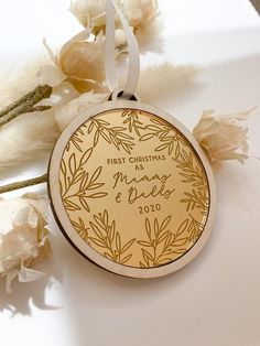 a christmas ornament hanging on a white table next to dried flowers and feathers