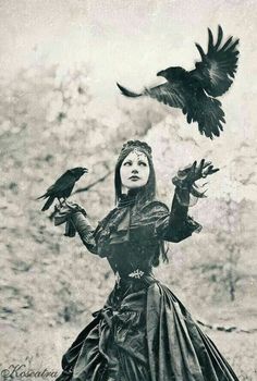 a woman in a long dress with two birds on her arm and one bird flying above her head