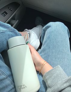 a person sitting in the back seat of a car holding a coffee cup and a travel mug