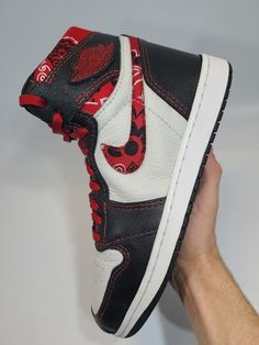 a hand holding up a pair of black and white sneakers with red print on them