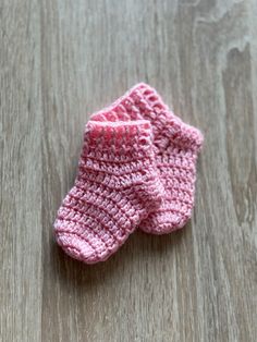 two pink crocheted baby booties sitting on top of a wooden floor