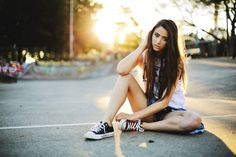 a young woman sitting on the ground with her hands behind her head and looking at the camera