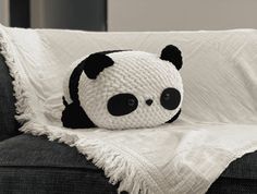 a crocheted panda bear sitting on top of a couch next to a blanket