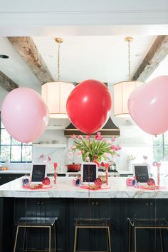 pink and red balloons are hanging from the ceiling above a kitchen island with bar stools