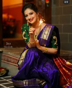 a woman in a purple and green sari holding a lit candle while sitting on the ground