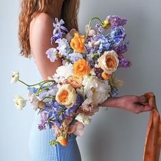 a woman in a blue dress holding a bouquet of white and orange flowers on her arm