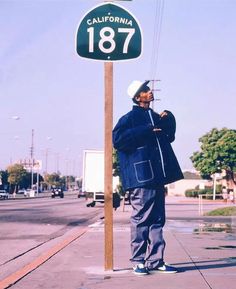 a man standing on the sidewalk next to a street sign that says california, 1876