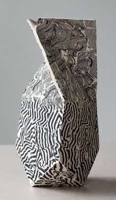 an artistically designed vase sitting on top of a wooden table next to a gray wall