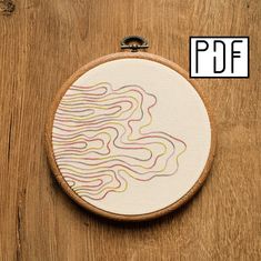 an embroidery project on a wooden table with a white circle and colorful lines in the middle