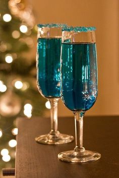 two wine glasses filled with green liquid sitting on a table next to a christmas tree