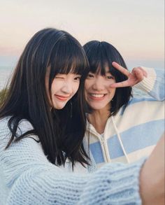 two young women taking a selfie with their cell phone in front of the ocean